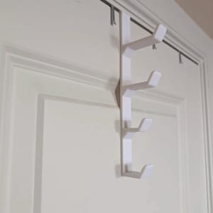 May include: A white over-the-door hook rack featuring a vertical bar with four evenly spaced, upward-angled hooks. The rack is constructed from a solid material and is designed to hang securely over the top edge of a standard interior door.