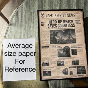 May include: A framed newspaper print titled UNSC INFINITY NEWS with a sepia-toned vintage aesthetic. The headline reads HERO OF REACH SAVES COUNTLESS, featuring illustrations of Master Chief and Covenant characters alongside various news columns.