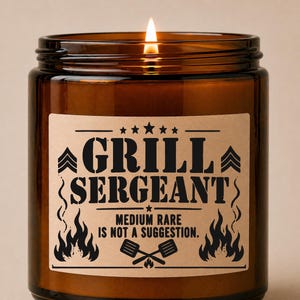 以下が含まれることがあります： 「GRILL SERGEANT」の文字が書かれたラベルが付いた、火の灯った茶色のガラスキャンドル。ラベルには「MEDIUM RARE IS NOT A SUGGESTION」の文字と炎と交差したグリルツールのグラフィックも含まれています。キャンドルはインテリアアイテムです。