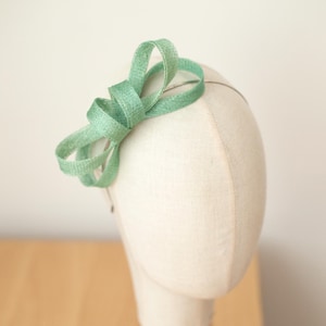 Peut inclure: Un serre-tête en tissu vert clair avec un nœud sur une tête de mannequin blanche. Le serre-tête est fait d'un tissu doux et délicat et est parfait pour ajouter une touche d'élégance à n'importe quelle tenue.
