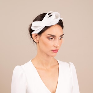 May include: A white fabric headband with a large bow on top. The headband is worn by a person with dark hair.