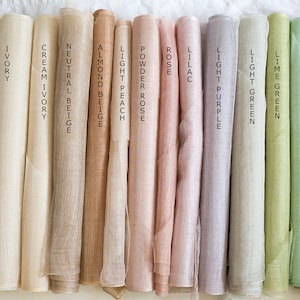 May include: A collection of fifteen fabric rolls arranged side-by-side, featuring a spectrum of colors labeled as white, light ivory, ivory, cream ivory, neutral beige, almond beige, light peach, powder rose, rose, lilac, light purple, light green, lime green, mint, jade, and petroleum.