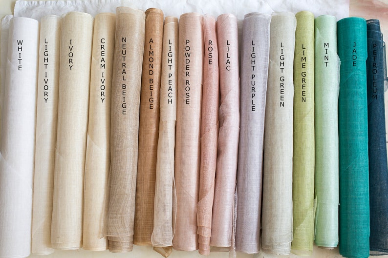 May include: A collection of fifteen fabric rolls arranged side-by-side, featuring a spectrum of colors labeled as white, light ivory, ivory, cream ivory, neutral beige, almond beige, light peach, powder rose, rose, lilac, light purple, light green, lime green, mint, jade, and petroleum.