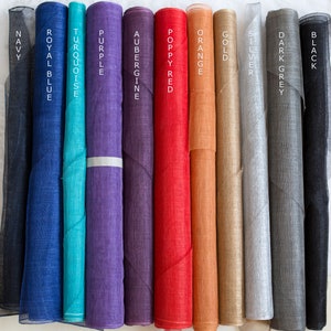 May include: Eleven vertical rolls of sheer fabric in various colors, labeled with text: Navy, Royal Blue, Turquoise, Purple, Aubergine, Poppy Red, Orange, Gold, Silver, Dark Grey, and Black. Each roll displays a fine, semi-transparent texture.