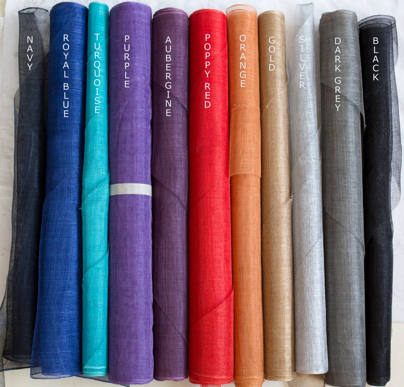 May include: Eleven vertical rolls of sheer fabric in various colors, labeled with text: Navy, Royal Blue, Turquoise, Purple, Aubergine, Poppy Red, Orange, Gold, Silver, Dark Grey, and Black. Each roll displays a fine, semi-transparent texture.