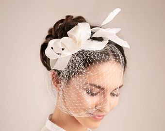 May include: A white bridal veil with a white bow and feathers attached. The veil is made of a fine mesh material and is worn over the bride's hair.