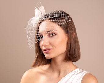 May include: A white bridal headpiece featuring a delicate net veil and a floral accent. The headpiece is designed with a fine mesh and a decorative flower, perfect for weddings or special occasions. The headpiece is a classic accessory for brides.
