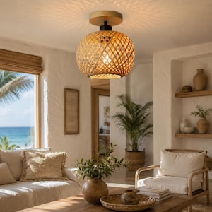 Puede incluir: Una lámpara colgante redonda de mimbre tejido. La lámpara está suspendida de un soporte de techo de madera. La habitación tiene una temática costera, con vistas al mar a través de una gran ventana. La luz proyecta un patrón en el techo.