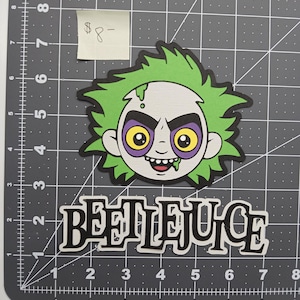 Puede incluir: Imagen de dibujos animados de Beetlejuice con pelo verde, cara gris y ojos amarillos con contornos morados. La palabra "BEETLEJUICE" está escrita en letras negras debajo de la cara del personaje. La imagen está sobre una cuadrícula gris.
