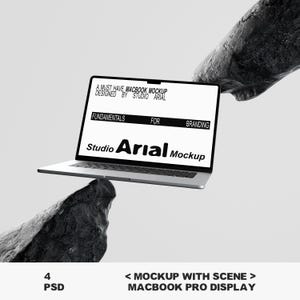 May include: A silver MacBook Pro display with the text "A MUST HAVE MACBOOK MOCKUP DESIGNED BY STUDIO ARIAL" and "FUNDAMENTALS FOR BRANDING". The screen also displays "Studio Arial Mockup". The laptop is set against a textured, dark grey background.