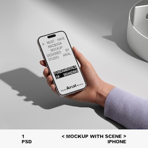 May include: A smartphone mockup held in a hand, displaying text that reads "A MUST HAVE MACBOOK MOCKUP DESIGNED BY STUDIO ARIAL FUNDAMENTALS OF BRANDING". The phone is silver with a black screen. The background is a light gray.