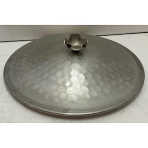May include: A round, silver-colored metal lid with a hammered texture across its surface. The lid features a central handle shaped like a small, open flower bud with layered petals, providing a decorative grip for lifting the cover.