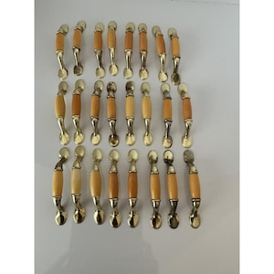May include: A collection of vintage cabinet pulls. Each pull features a light-colored, cylindrical wooden handle with a brass-toned base and a decorative, spoon-shaped end. The handles vary in color from light to medium brown.
