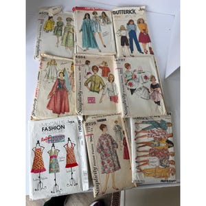 May include: A collection of vintage sewing patterns from brands like Simplicity, Butterick, and McCall's. The patterns feature illustrations of dresses, aprons, and other garments. The covers are colorful, with text such as "Retro Aprons" and "Fast & Easy".