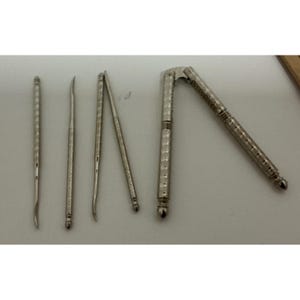 May include: A set of silver-toned metal seafood tools including four slender, textured picks with curved ends and one hinged nutcracker with a matching ridged design. The tools are arranged in a row, showcasing their metallic finish and detailed, grooved handles for a secure grip during use.