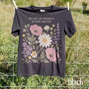 Könnte beinhalten: Ein anthrazitfarbenes Kurzarm-T-Shirt mit dem weißen Text NO ACT OF KINDNESS IS EVER WASTED über einer grafischen Illustration verschiedener Blumen, darunter rosa Mohnblumen, ein großes weißes Gänseblümchen sowie kleine violette und gelbe Blüten.