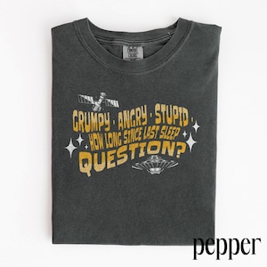May include: Dark grey t-shirt with the text "GRUMPY. ANGRY. STUPID. HOW LONG SINCE LAST SLEEP QUESTION?" in yellow and white. The shirt features a satellite and a UFO graphic.