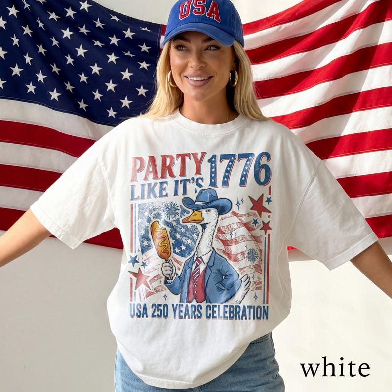 May include: White t-shirt with a patriotic design featuring a goose in a suit holding a corn dog, with the text "PARTY LIKE IT'S 1776" and "USA 250 YEARS CELEBRATION". The design incorporates red, white, and blue colors.