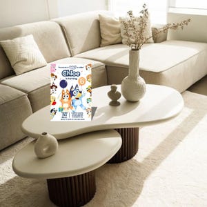 May include: A birthday party invitation featuring the characters Bluey and Bingo. The invitation reads "Chloe is turning 6" with the date and time of the party. The invitation is on a white table with a beige sofa in the background.