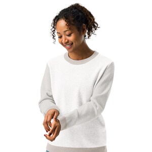 May include: A white and light gray sweatshirt with a crew neck and long sleeves. The sleeves and trim are light gray, while the body is white. The person is wearing the sweatshirt and smiling.