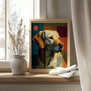 Op de afbeelding: Een ingelijste kunstdruk met een gestileerd portret van een gele Labrador Retriever. Het kunstwerk maakt gebruik van geometrische vormen en een kleurenpalet van geel, blauw en oranje. De print wordt weergegeven op een houten oppervlak bij een raam.