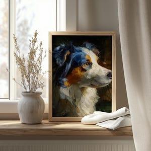 Op de afbeelding: Een ingelijst olieverfschilderij van een hond met blauwe, witte en bruine vacht. De hond staat in profiel, met een geconcentreerde blik. Het kunstwerk wordt tentoongesteld op een houten vensterbank, naast een vaas met gedroogde planten.
