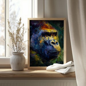 Op de afbeelding: Een ingelijste kunstafdruk van een gorilla's gezicht, weergegeven in een kleurrijke, impressionistische stijl. Het kunstwerk gebruikt blauw, geel en groen, met de nadruk op de intense blik van de gorilla. De lijst is licht van kleur.