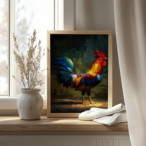 Op de afbeelding: Een ingelijst schilderij van een kleurrijke haan met een rode kam, een gele en oranje lichaam en blauwe en groene staartveren. Het kunstwerk wordt tentoongesteld op een houten vensterbank naast een vaas met gedroogde planten.