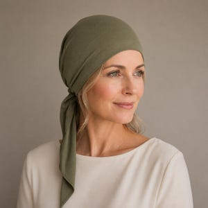Può includere: Un copricapo color verde oliva realizzato in tessuto morbido che copre la sommità del capo, caratterizzato da un design liscio e aderente con un singolo laccio in tessuto che pende sul lato sinistro, offrendo copertura totale e una tenuta sicura.
