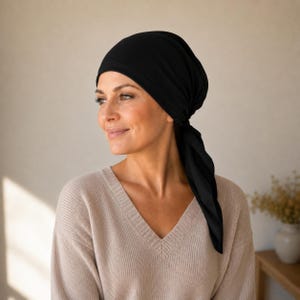 May include: A solid black head scarf tied securely around the head, featuring a smooth fabric texture and a pointed tail that hangs down on one side. The head covering is opaque and provides full coverage, wrapping snugly to create a clean silhouette.