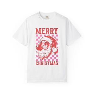 Puede incluir: Camiseta blanca con un gráfico rojo y rosa. El gráfico presenta la cara de Papá Noel con gafas de sol en forma de corazón y una burbuja de chicle. Las palabras "MERRY CHRISTMAS" están impresas arriba y abajo de la cara de Papá Noel.