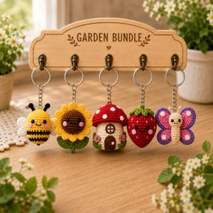 Può includere: Un portachiavi in legno con la scritta "GARDEN BUNDLE" contiene cinque portachiavi all'uncinetto. I portachiavi includono un'ape, un girasole, una casa a fungo, una fragola e una farfalla. Ogni portachiavi è attaccato a un anello di metallo.