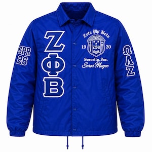 May include: A royal blue coach jacket featuring white screen-printed graphics. The front displays the Greek letters ZΦB, the Zeta Phi Beta Sorority, Inc. crest with the text 1920 and Soror Magee, while the sleeves show SPR 26 and ΩΛΖ.