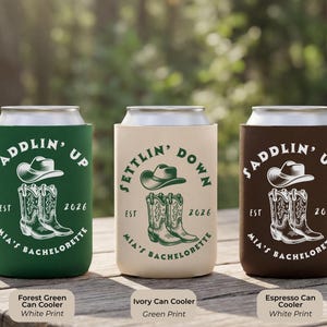 Puede incluir: Tres enfriadores de latas en verde bosque, marfil y espresso. Cada uno presenta un sombrero de vaquero y botas con el texto "Saddlin' Up" o "Settlin' Down", "Mia's Bachelorette" y el a&ntilde;o 2026.
