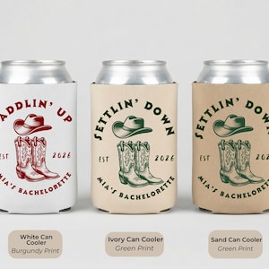 Puede incluir: Tres enfriadores de latas con dise&ntilde;os tem&aacute;ticos de vaqueros. El enfriador blanco tiene una impresi&oacute;n burdeos con un sombrero y botas de vaquero, el texto dice "Saddlin' Up". Los enfriadores marfil y arena tienen una impresi&oacute;n verde con un sombrero y botas de vaquero, el texto dice "Settlin' Down".