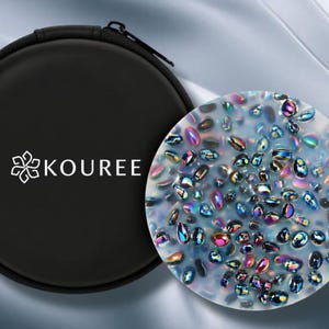 May include: A black, round case with the white text "KOUREE" and a floral design. Next to it is a round, clear object filled with iridescent, colourful, oval-shaped stones. The background is a light grey, silky fabric.