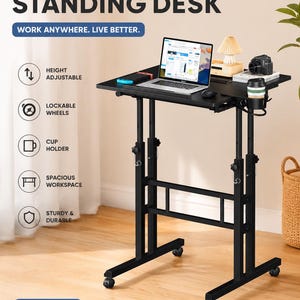 May include: A black mobile standing desk with height-adjustable legs, lockable wheels, and a built-in cup holder. The desk surface holds a laptop, a small lamp, and a camera. Text on the image includes MOBILE STANDING DESK, HOLDS UP TO 110 LBS.