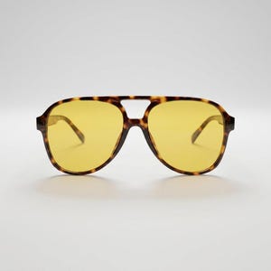 May include: Aviator-style sunglasses with a tortoiseshell frame and yellow lenses. The sunglasses have a double bridge and a classic, retro design. The lenses are a bright yellow color, and the frame has a brown and tan pattern.