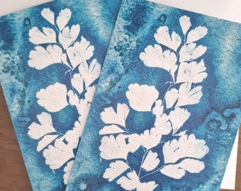 Puede incluir: Dos tarjetas de felicitación con diseños de hojas de helecho blancas sobre un fondo azul acuarela. Las tarjetas van acompañadas de sobres blancos. Las tarjetas tienen un tema botánico.