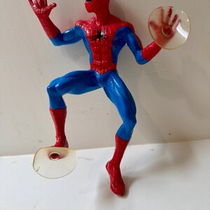 May include: A Spider-Man action figure in a dynamic pose, featuring a red and blue costume. The figure has a red mask with white eye lenses, a black spider emblem on the chest, and is holding a clear disc in one hand. The figure is approximately 6 inches tall.