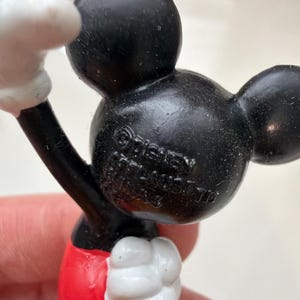 May include: A close-up of a Mickey Mouse figurine. The figurine has a black head and ears, a red bottom, and white gloves. The text "&copy; Disney" is visible on the back of the head.