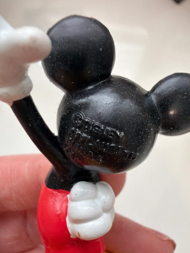 May include: A close-up of a Mickey Mouse figurine. The figurine has a black head and ears, a red bottom, and white gloves. The text "&copy; Disney" is visible on the back of the head.