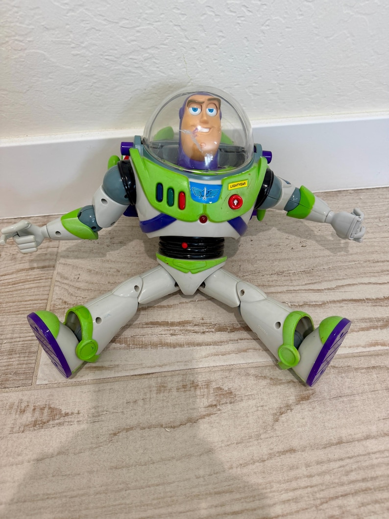 May include: A Buzz Lightyear action figure from the Toy Story franchise. The toy is primarily white, green, and purple, with a clear plastic helmet. The figure has articulated limbs and is posed with arms and legs spread.