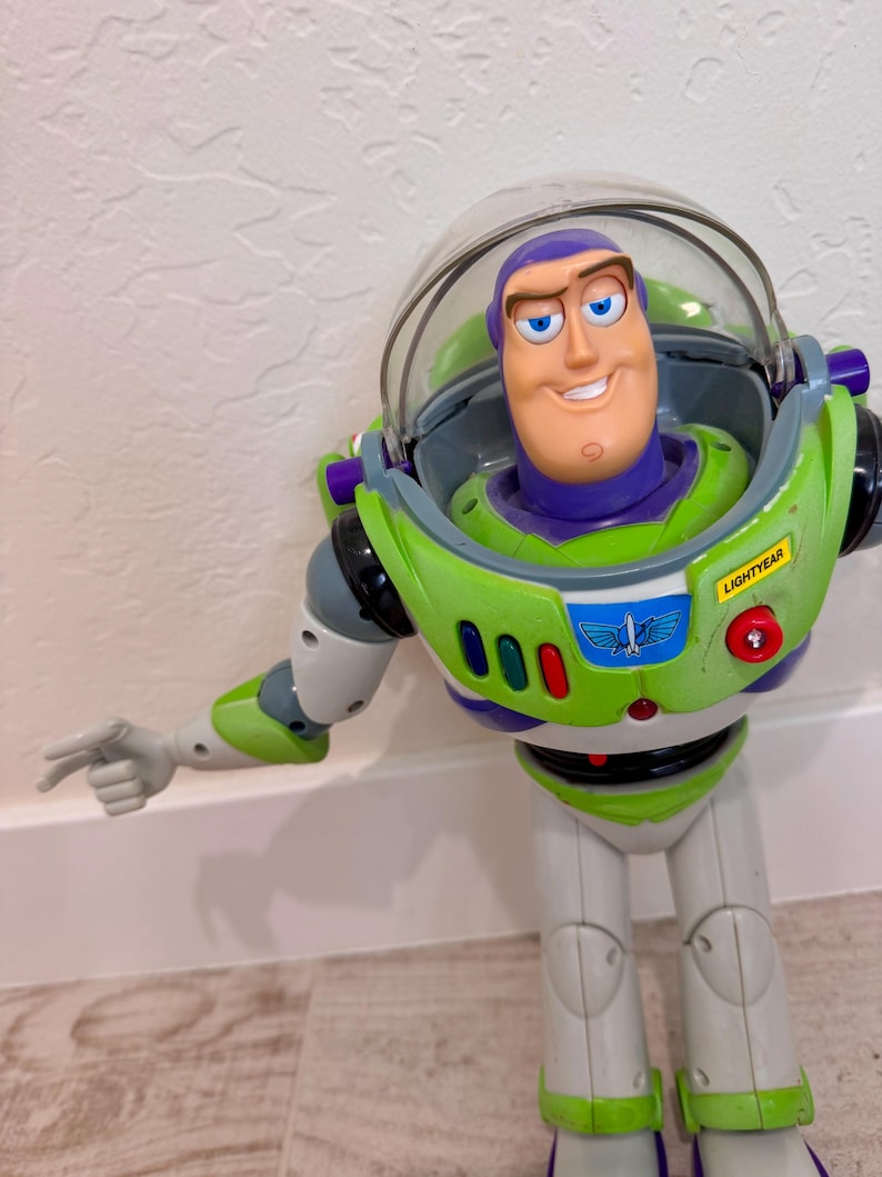 May include: A Buzz Lightyear action figure in a classic green, white, and purple spacesuit. The toy has a clear helmet, a smiling face, and the word "LIGHTYEAR" on the chest. The figure is pointing with its left arm.