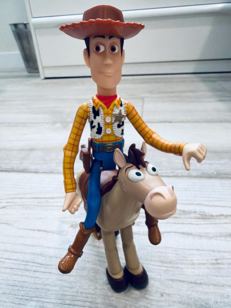 May include: A Woody action figure from the Toy Story franchise. The figure is wearing a brown cowboy hat, yellow plaid shirt, vest, blue trousers, and brown boots. Woody is riding a brown and tan horse.