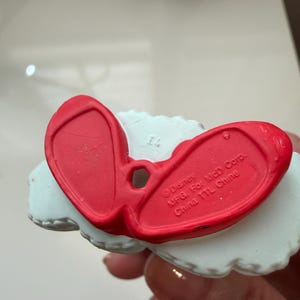 May include: A close-up of the bottom of a red and white figurine. The red portion is shaped like a pair of shoes. The text "Disney MFG. For McD Corp. China TTL Chine" is visible on the red portion.