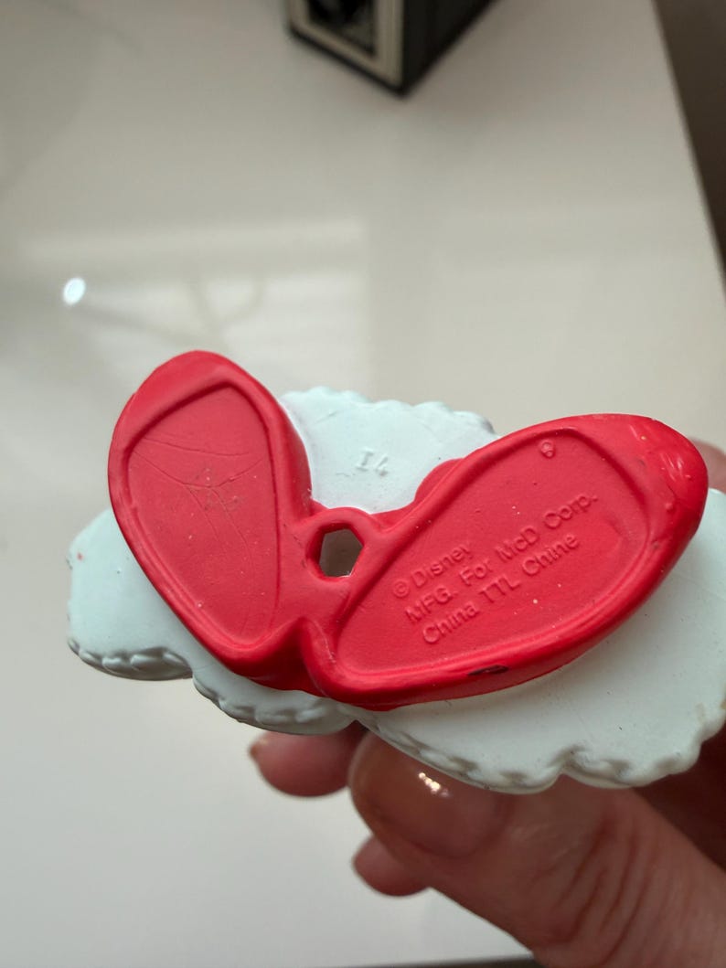 May include: A close-up of the bottom of a red and white figurine. The red portion is shaped like a pair of shoes. The text "Disney MFG. For McD Corp. China TTL Chine" is visible on the red portion.