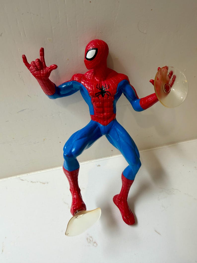 May include: A Spider-Man action figure in a dynamic pose, featuring a red and blue costume with a black spider emblem on the chest. The figure has a red mask with white eye lenses and is holding a clear disc. The figure is approximately 6 inches tall.