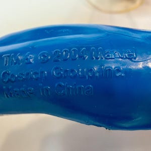 May include: Close-up of a blue plastic toy with embossed text. The text includes "TM & &copy; 2004 Marvel Cosrich Group, Inc. Made in China."