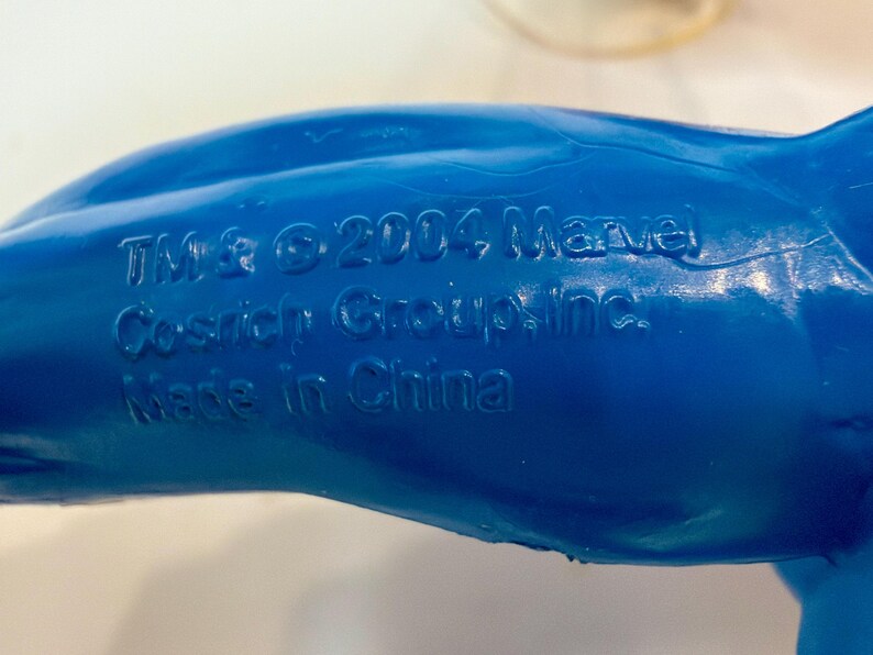 May include: Close-up of a blue plastic toy with embossed text. The text includes "TM & &copy; 2004 Marvel Cosrich Group, Inc. Made in China."